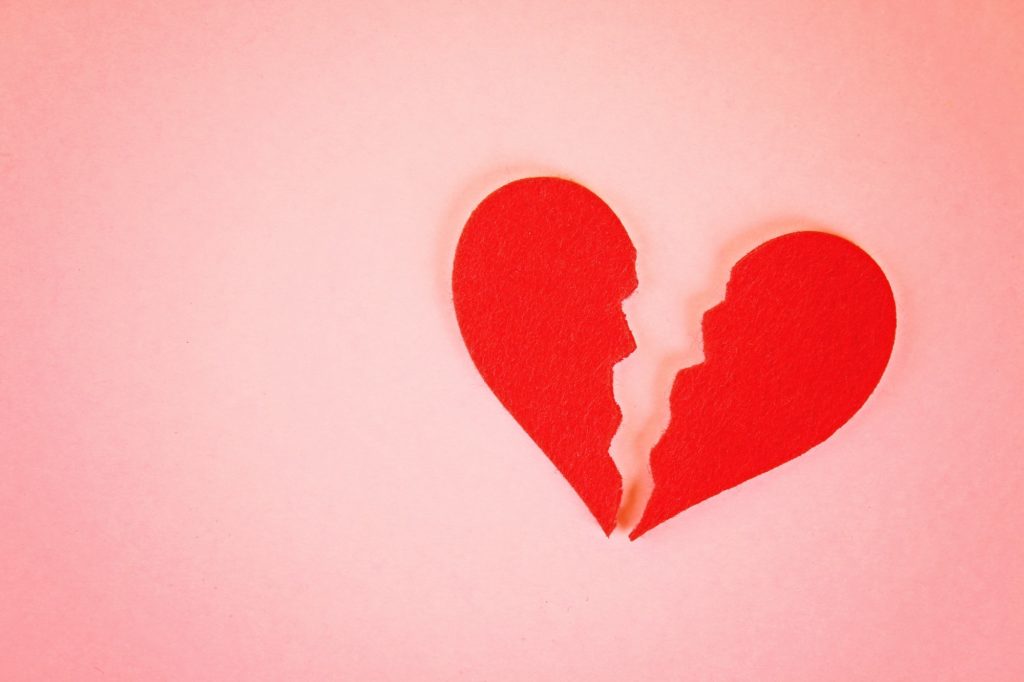 Red felt heart broken into two halves on a pink background.